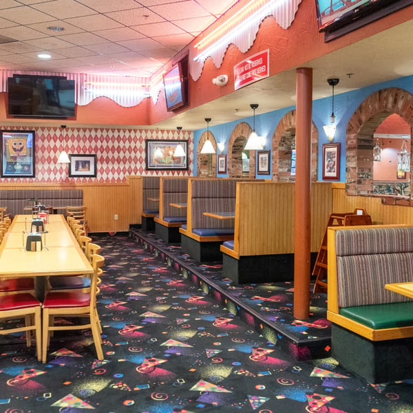 A colorful, empty restaurant dining room with booths, tables, and a pizza-themed carpet.