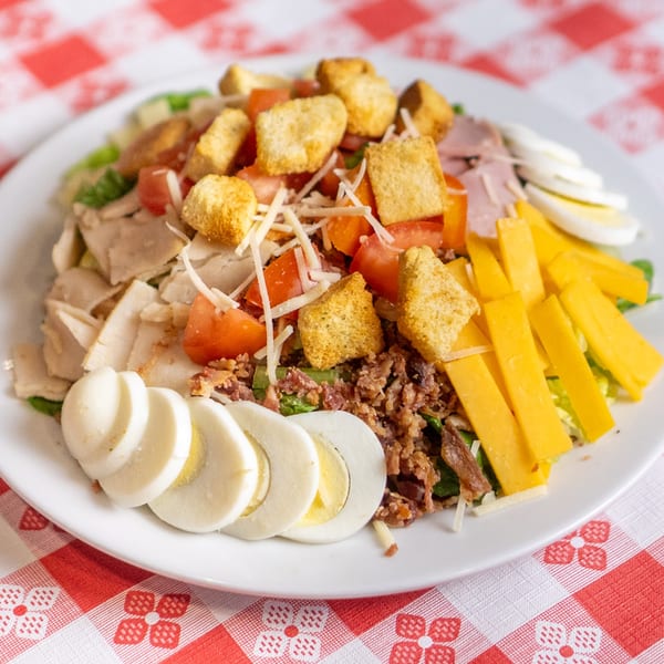 A vibrant chef salad with chicken, ham, cheese, tomatoes, croutons, bacon bits, and sliced eggs.