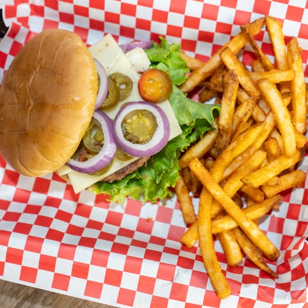 Overhead view of a burger with cheese, red onion, and jalapeños, served with fries in a red checkered basket.
