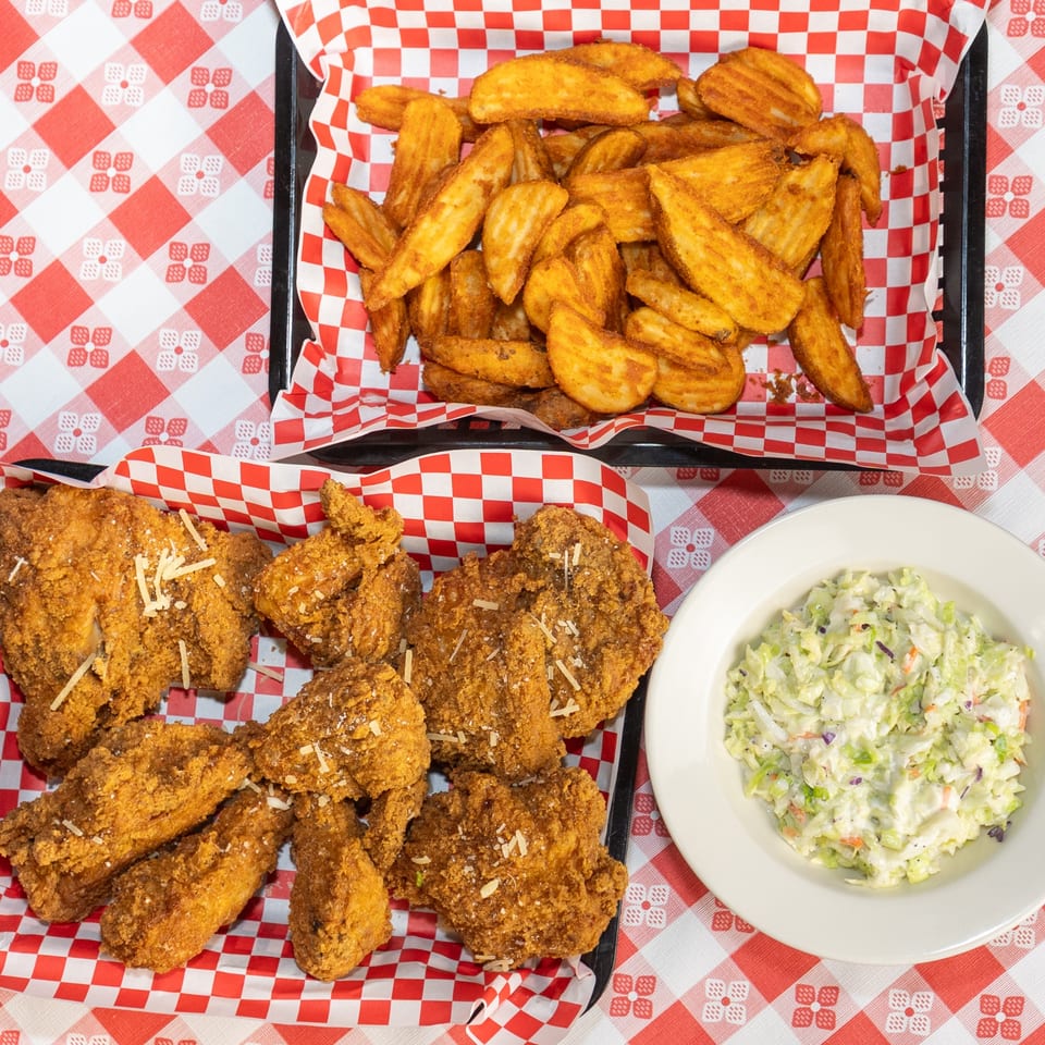 Fried chicken, potato wedges, and coleslaw on a red and white checkered tablecloth.