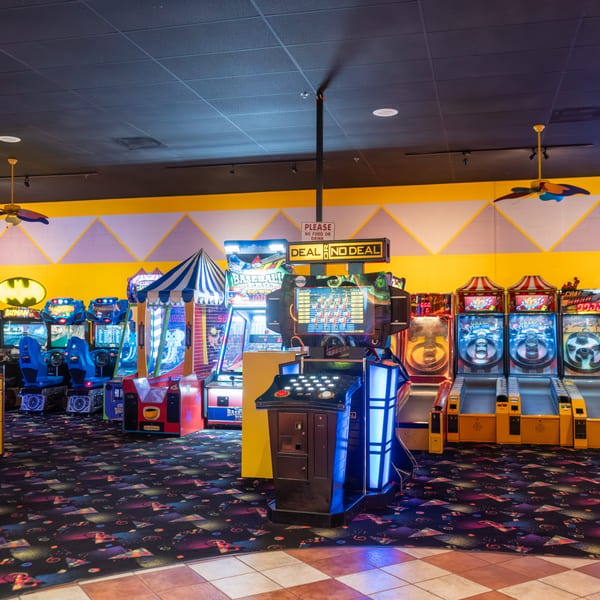 A vibrant arcade room with numerous colorful game machines, including "Deal or No Deal" and Skee-Ball.