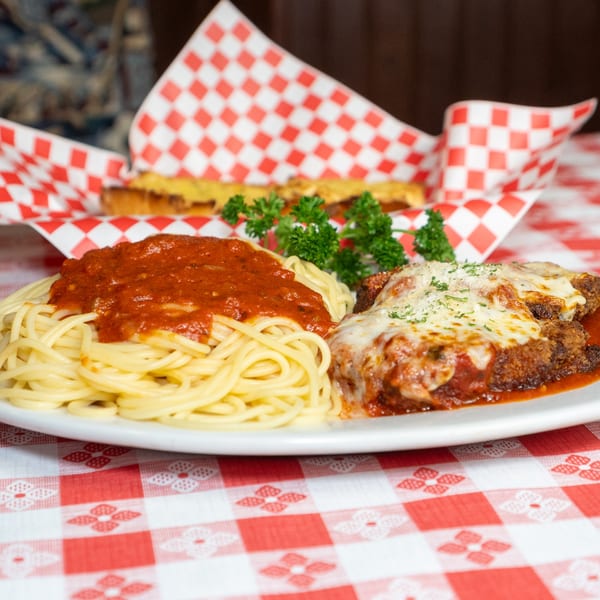 Spaghetti with red sauce, chicken parmesan, and garlic bread in a red checkered basket.