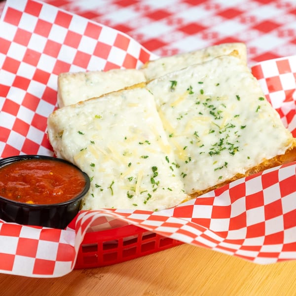 Cheesy garlic bread with parsley and parmesan in a red and white checkered basket with marinara.
